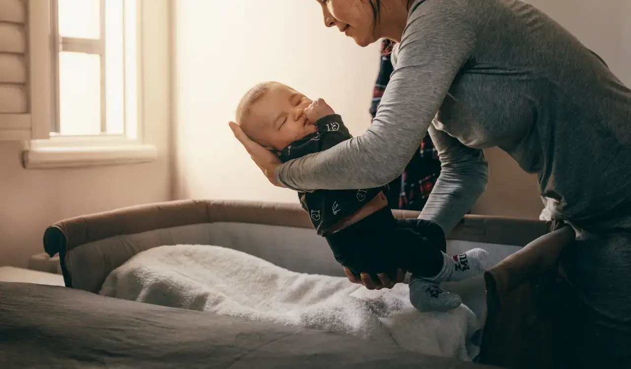 Picture of a mother laying her child in bed for a no bed bugs here ad.